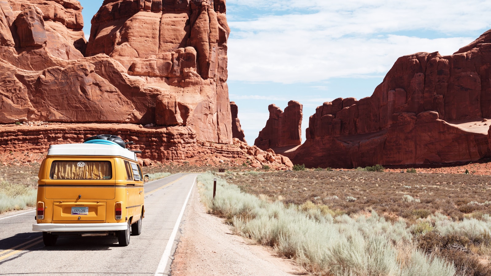Open road through American desert landscape with red rocks and cloud-streaked sky
